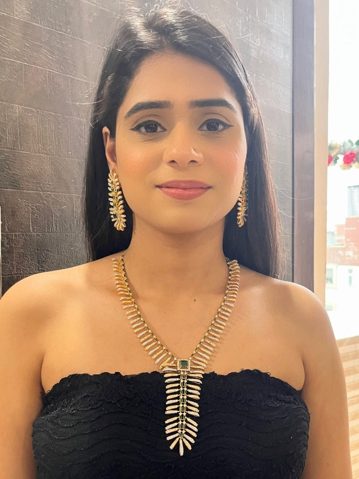 A woman in a strapless black dress showcases the Selvaggia long Necklace Set, featuring sparkling American Diamonds and white stones, with large earrings and an intricate green necklace adorned with gemstone accents.