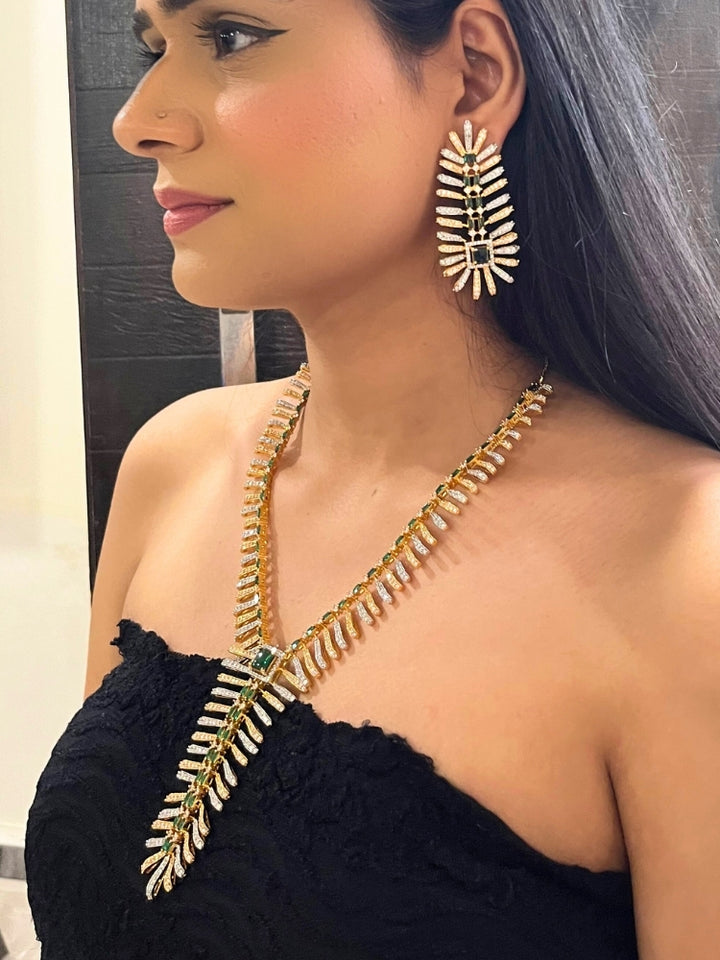 A woman in a strapless black dress showcases the Selvaggia long Necklace Set, featuring sparkling American Diamonds and white stones, with large earrings and an intricate green necklace adorned with gemstone accents.