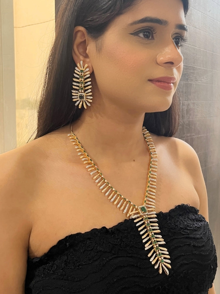 A woman in a strapless black dress showcases the Selvaggia long Necklace Set, featuring sparkling American Diamonds and white stones, with large earrings and an intricate green necklace adorned with gemstone accents.