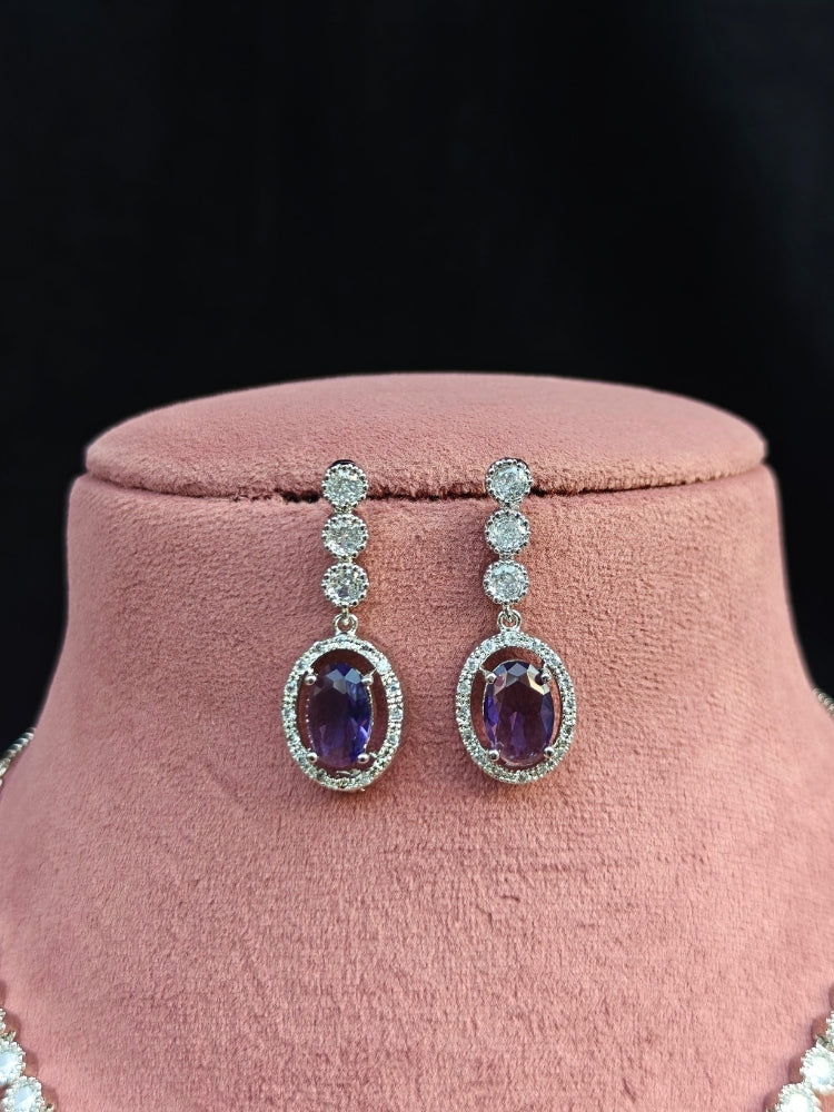 Close-up of a woman wearing an ornate Western Purple (Silver Gold) Collar jewellery set and earrings with American Diamond and Colored Stones. Reception-ready look featuring a statement American diamond jewelry set. Close-up of a cocktail party look featuring a premium American diamond necklace.
