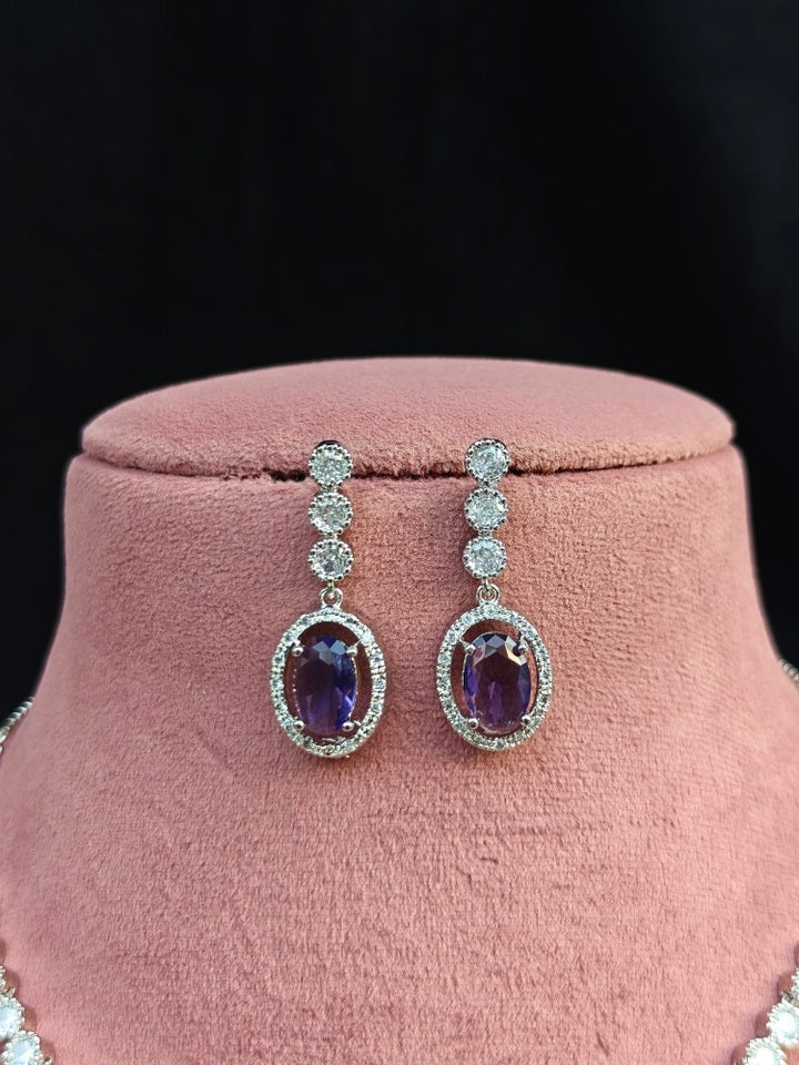 Close-up of a woman wearing an ornate Western Purple (Silver Gold) Collar jewellery set and earrings with American Diamond and Colored Stones. Reception-ready look featuring a statement American diamond jewelry set. Close-up of a cocktail party look featuring a premium American diamond necklace.