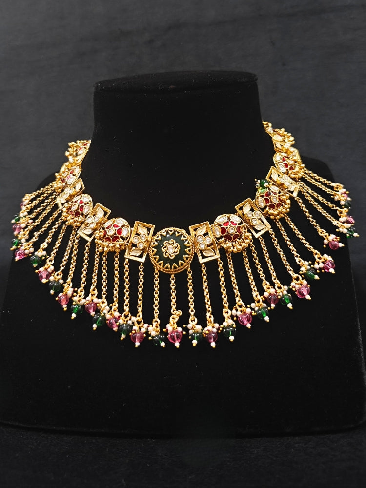 Close-up of an ornate traditional Red and Green Heritage gold Collar jewellery set and earrings and maangtikka with Beads, Colored Stones and Kundan. A heritage-inspired artificial necklace for wedding festivities. Saree styling inspiration with a traditional heritage necklace.