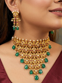 Close-up of a women wearing an ornate traditional (Gold Polish) Choker jewellery set and earrings with Pearls, Green Beads and Colored Stones. Wedding guest look featuring a statement imitation jewelry set. Wedding guest outfit enhanced with elegant artificial jewelry.