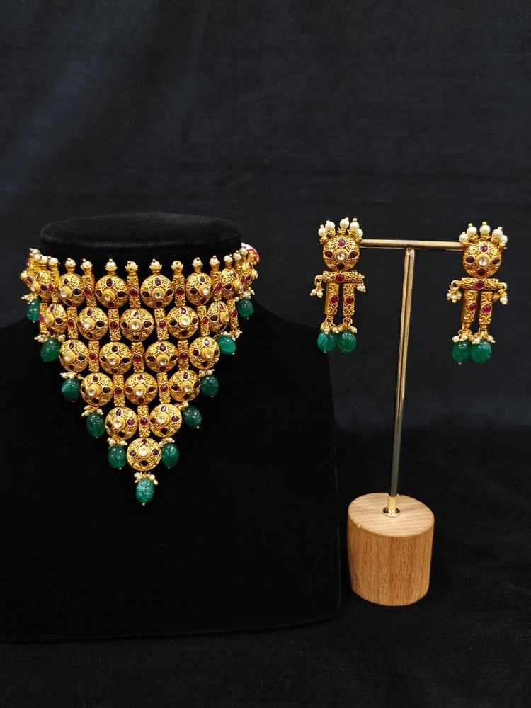 Close-up of an ornate traditional (Gold Polish) Choker jewellery set and earrings with Pearls, Green Beads and Colored Stones. Wedding guest look featuring a statement imitation jewelry set. Wedding guest outfit enhanced with elegant artificial jewelry.