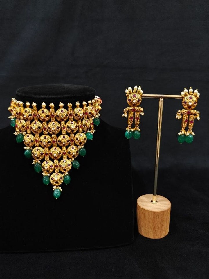 Close-up of an ornate traditional (Gold Polish) Choker jewellery set and earrings with Pearls, Green Beads and Colored Stones. Wedding guest look featuring a statement imitation jewelry set. Wedding guest outfit enhanced with elegant artificial jewelry.