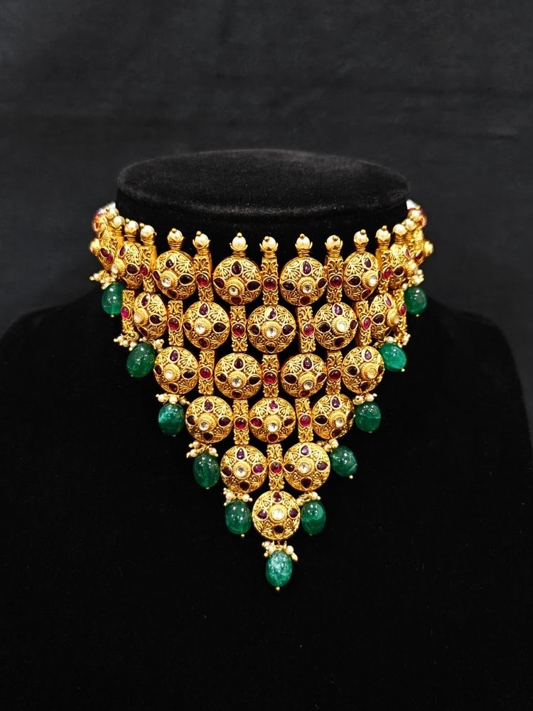 Close-up of an ornate traditional (Gold Polish) Choker jewellery set and earrings with Pearls, Green Beads and Colored Stones. Wedding guest look featuring a statement imitation jewelry set. Wedding guest outfit enhanced with elegant artificial jewelry.