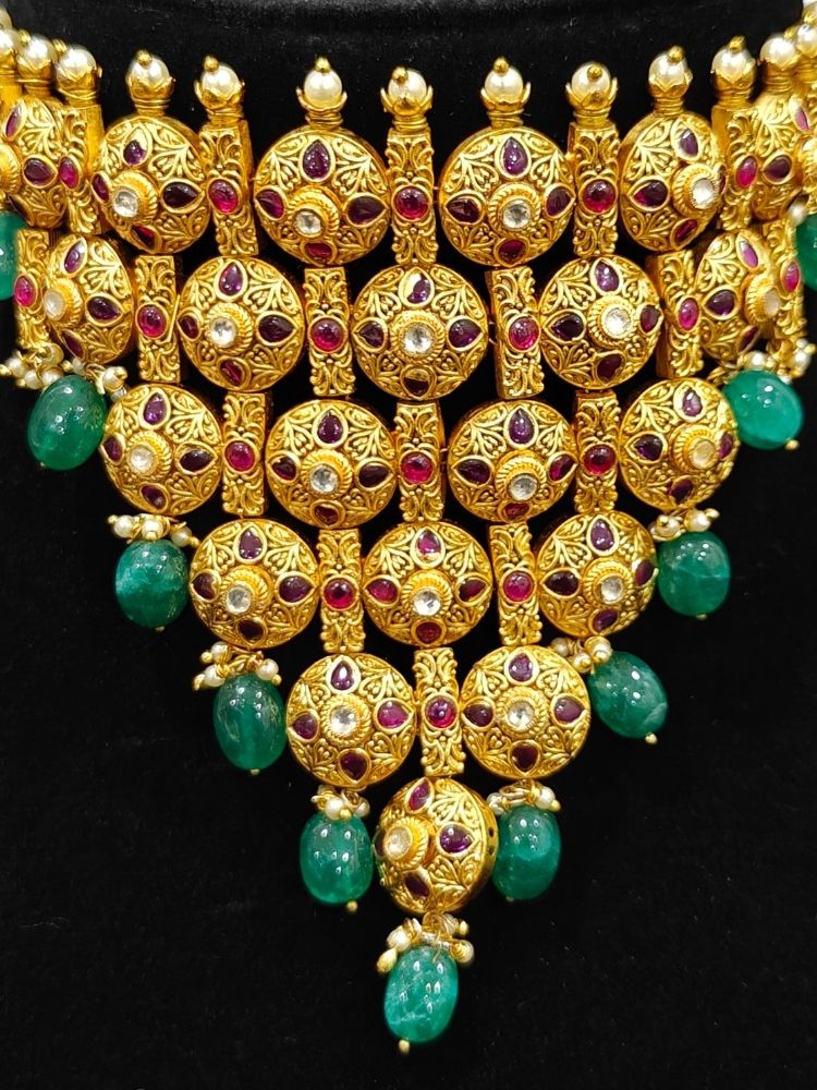 Close-up of an ornate traditional (Gold Polish) Choker jewellery set and earrings with Pearls, Green Beads and Colored Stones. Wedding guest look featuring a statement imitation jewelry set. Wedding guest outfit enhanced with elegant artificial jewelry.