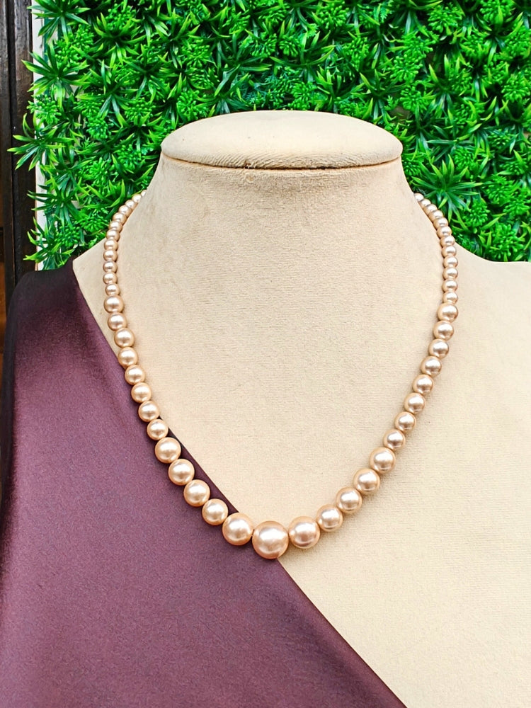 A mannequin in teal velvet showcases the Sharon champagne Necklace Set—a single-strand Champagne pearl necklace—elegantly draped with gold and beige embroidery on one shoulder, against a softly patterned background. Ideal for wedding ceremonies.
