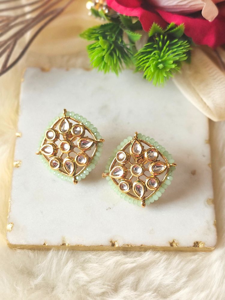 Sharvisha Mint Green Earrings: Square-shaped Kundan earrings with teardrop white Kundan accents, surrounded by Mint Green crystal stones, displayed on a marble-like surface with flowers in the background.