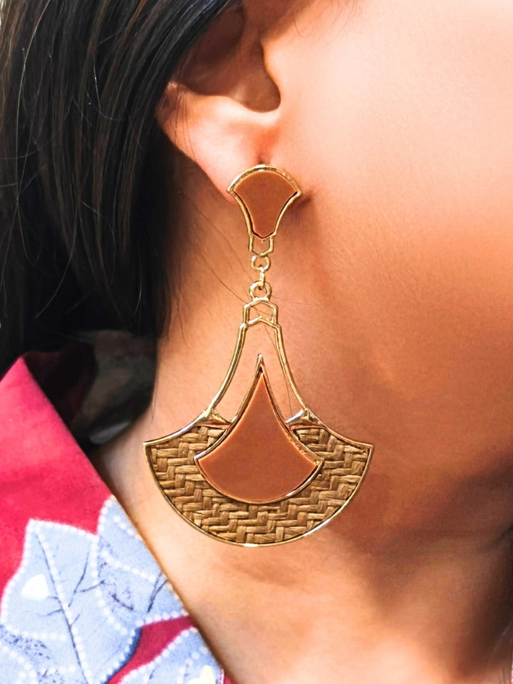 A close-up of a persons ear wearing Shefali Brown Earrings featuring gold geometric and woven jute details, paired with a red and blue patterned shirt.