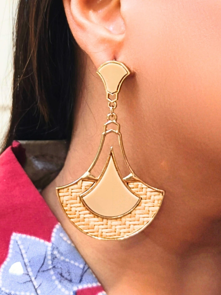A close-up of a persons ear wearing Shefali Cream Earrings featuring gold geometric and woven jute details, paired with a red and blue patterned shirt.