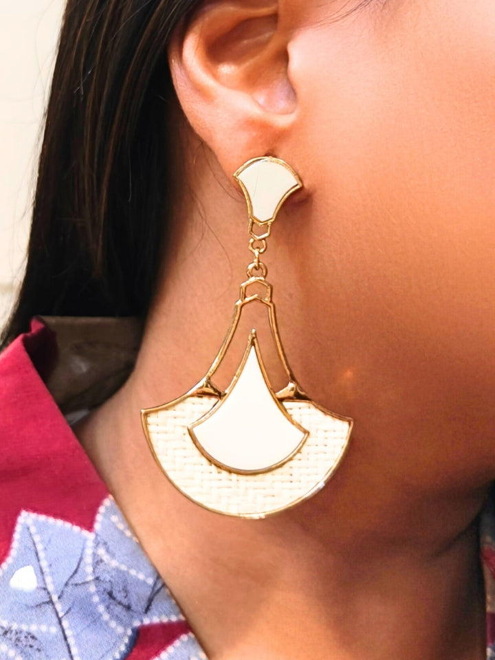 A close-up of a persons ear wearing Shefali White Earrings featuring gold geometric and woven jute details, paired with a red and blue patterned shirt.