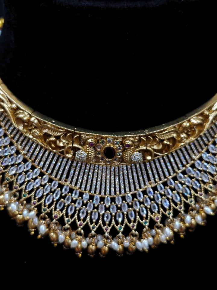 Close-up of an ornate traditional (Gold Polish) Choker jewellery set and earrings with American Diamond and Pearls. A woman wearing a luxury American diamond necklace set styled beautifully for a wedding guest look in India. Elegant wedding jewelry look featuring a premium artificial American diamond necklace.