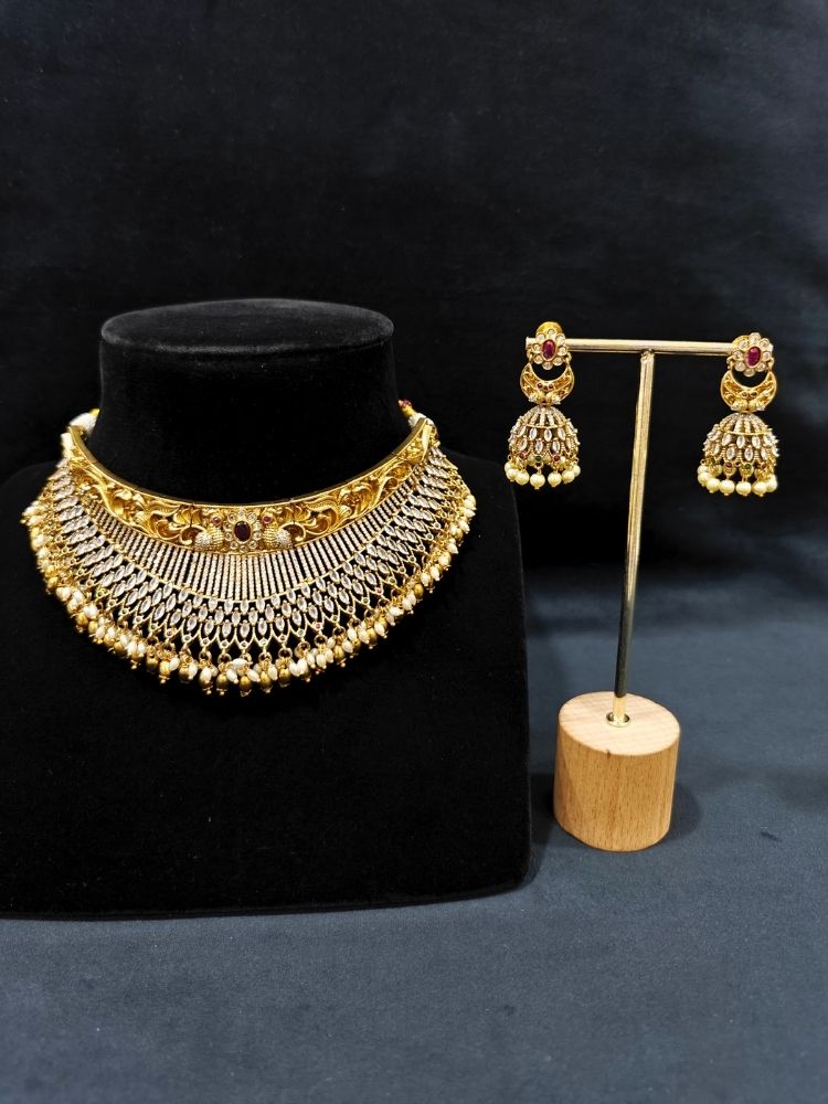 Close-up of an ornate traditional (Gold Polish) Choker jewellery set and earrings with American Diamond and Pearls. A woman wearing a luxury American diamond necklace set styled beautifully for a wedding guest look in India. Elegant wedding jewelry look featuring a premium artificial American diamond necklace.
