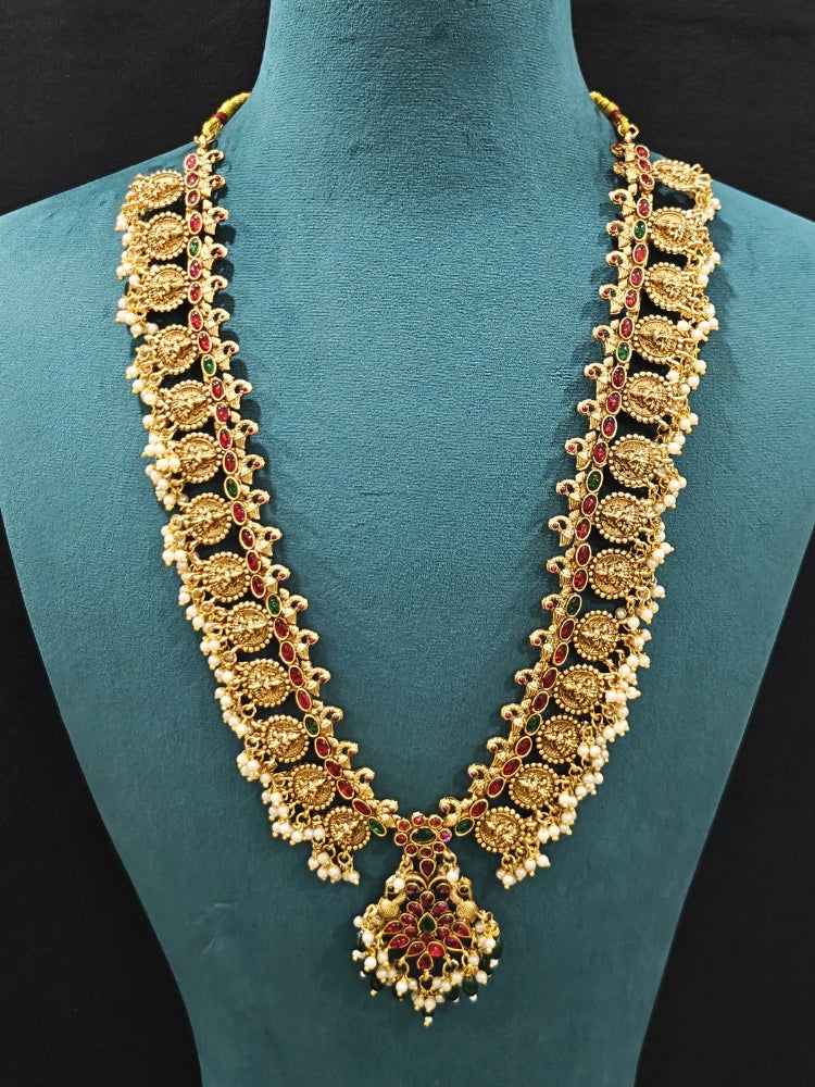The Shraddha Temple Necklace Set featuring a traditional gold Long necklace and matching earrings with   Pearls, Colored Stones and Mehendi Polish .  Close-up of detailed temple carvings in artificial wedding jewelry. Festive Diwali look completed with a traditional temple necklace set.