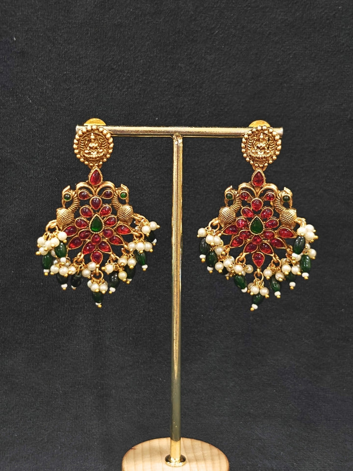 The Shraddha Temple Necklace Set featuring a traditional gold Long necklace and matching earrings with   Pearls, Colored Stones and Mehendi Polish .  Close-up of detailed temple carvings in artificial wedding jewelry. Festive Diwali look completed with a traditional temple necklace set.
