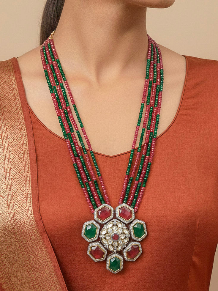 Close-up of a woman wearing an ornate traditional Diamond Ruby Red and Green jewellery set and earrings with Kundan, American Diamond, Monalisa Stones and Crystal Beads. A woman wearing a luxury American diamond necklace set styled beautifully for a wedding guest look in India. Elegant festive look with a high-quality imitation American diamond necklace set.