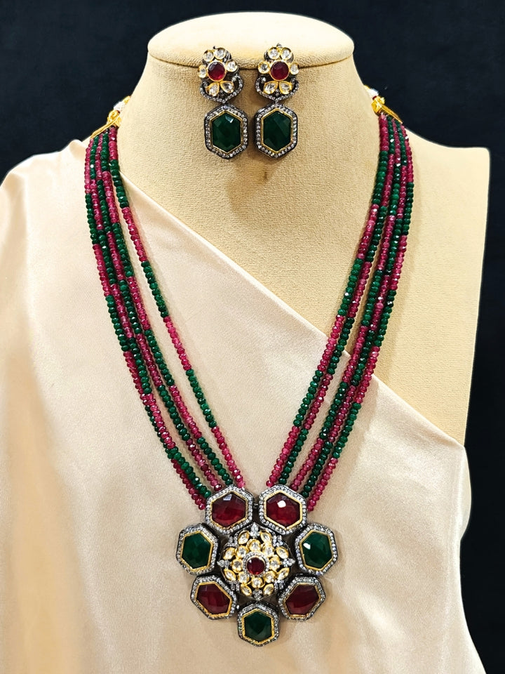 Close-up of an ornate traditional Diamond Ruby Red and Green jewellery set and earrings with Kundan, American Diamond, Monalisa Stones and Crystal Beads. A  luxury American diamond necklace set styled beautifully for a wedding guest look in India. Elegant festive look with a high-quality imitation American diamond necklace set.