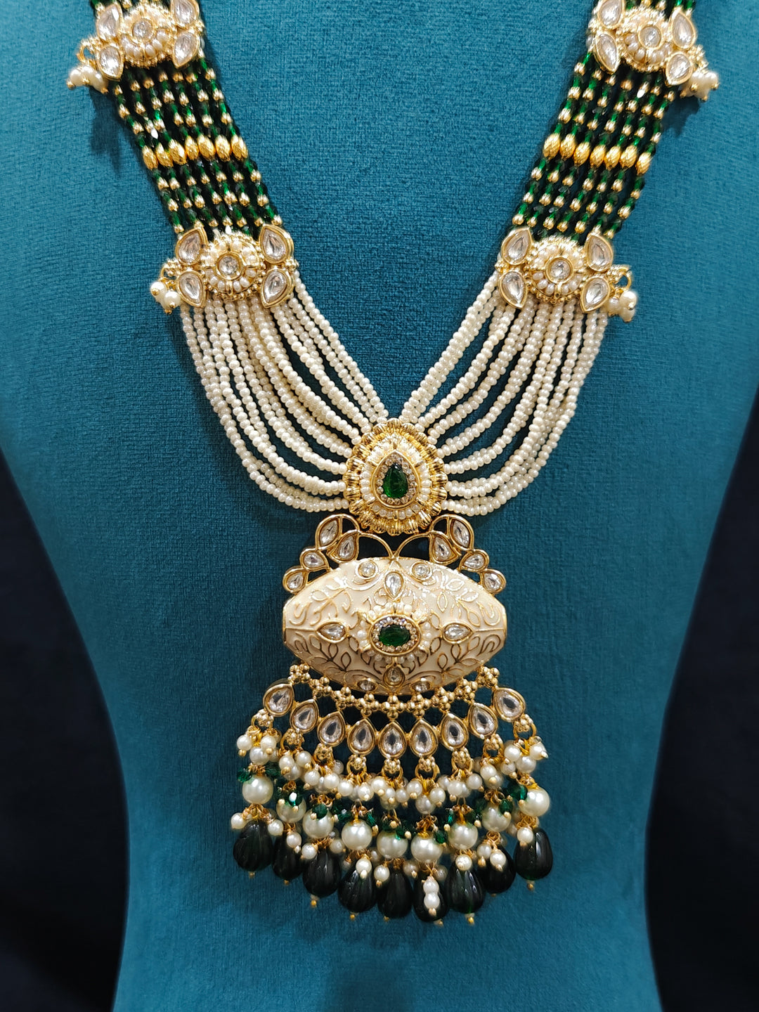 Close-up of a woman wearing an ornate traditional Dark Green Rajwadi gold Long jewellery set and earrings  with Pearls, Beads, Meenakari and Moissanite Kundan. Festive Diwali outfit enhanced with a Rajwadi artificial necklace. Close-up of a premium Rajwadi artificial necklace under 10000. Perfect Rajwadi necklace set for weddings and festivals.