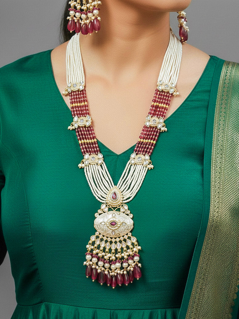 Close-up of a woman wearing an ornate traditional Ruby Pink Rajwadi gold Long jewellery set and earrings  with Pearls, Beads, Meenakari and Moissanite Kundan. Woman wearing a Rajwadi necklace for a reception function. Luxury imitation Rajwadi necklace worn for wedding celebrations.