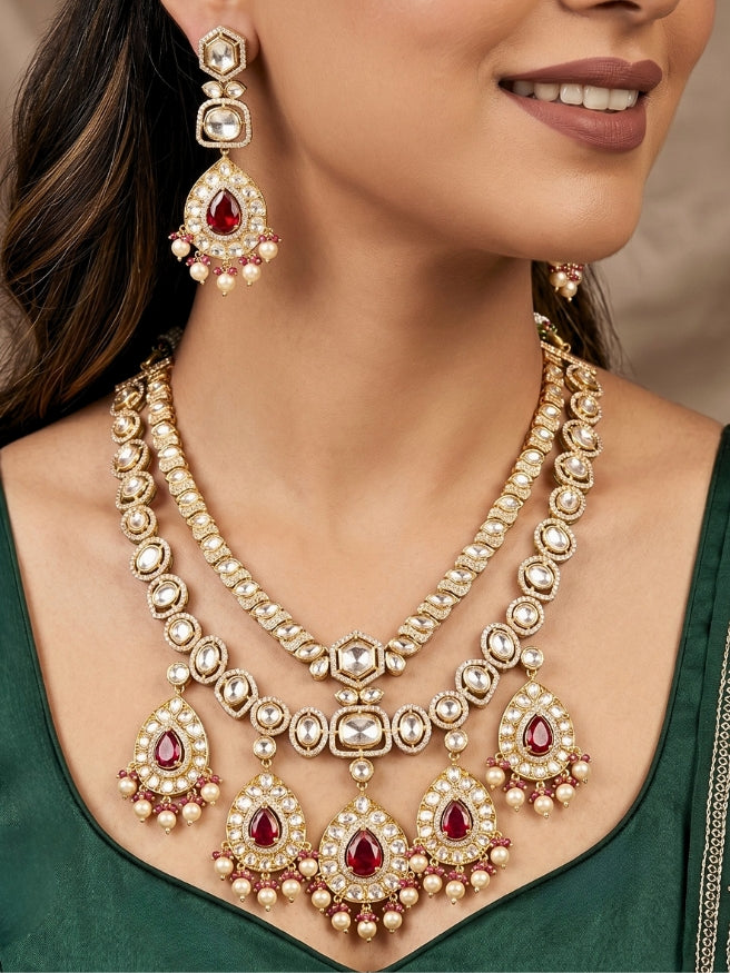 Close-up of a woman wearing an ornate traditional (Gold Polish) Layered Red jewellery set and earrings with Polki, American Diamond and Red Colored stones. Woman styling a premium Polki imitation necklace for wedding celebrations. Festive celebration look completed with premium imitation Polki jewelry.