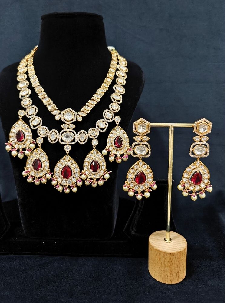 Close-up of an ornate traditional (Gold Polish) Layered Red jewellery set and earrings with Polki, American Diamond and Red Colored stones. Woman styling a premium Polki imitation necklace for wedding celebrations. Festive celebration look completed with premium imitation Polki jewelry.