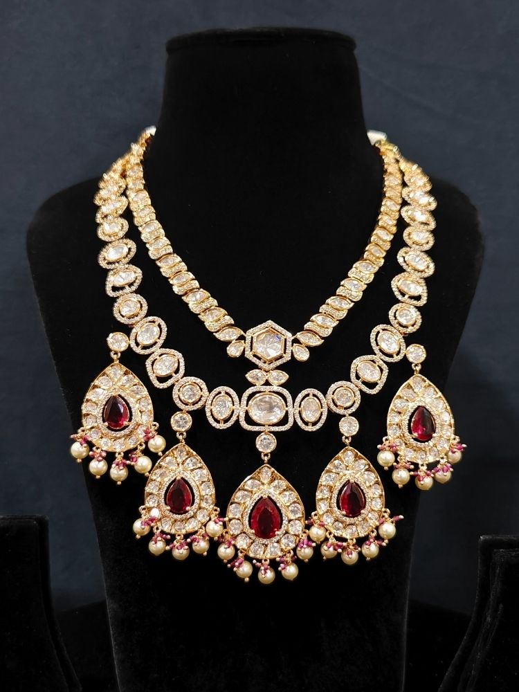 Close-up of an ornate traditional (Gold Polish) Layered Red jewellery set and earrings with Polki, American Diamond and Red Colored stones. Woman styling a premium Polki imitation necklace for wedding celebrations. Festive celebration look completed with premium imitation Polki jewelry.
