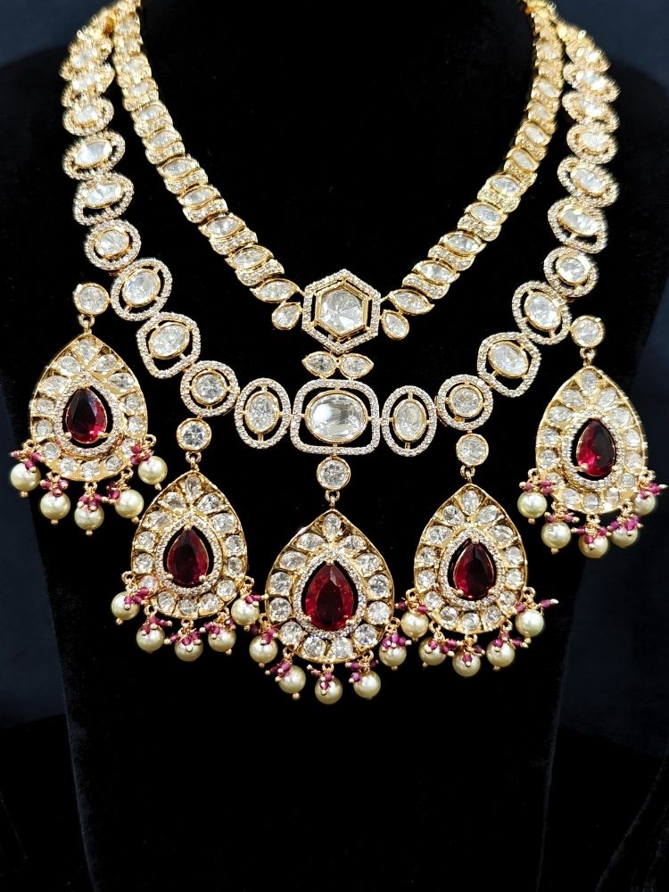 Close-up of an ornate traditional (Gold Polish) Layered Red jewellery set and earrings with Polki, American Diamond and Red Colored stones. Woman styling a premium Polki imitation necklace for wedding celebrations. Festive celebration look completed with premium imitation Polki jewelry.