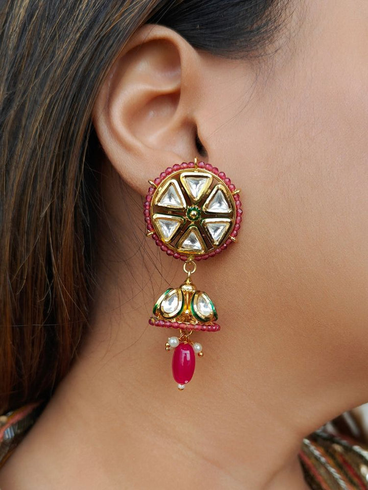 Close-up of a woman’s ear wearing the Sophie Earrings—large circular gold with Kundan stones, red crystal stones, a dangling jhumki, and a red bead—set against straight dark hair. Ideal for dressing up at weddings.