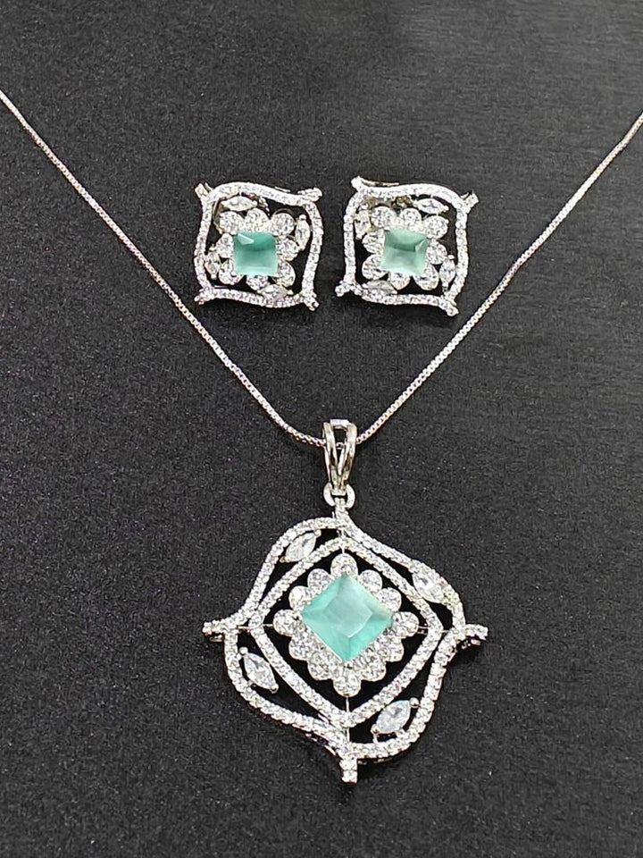 The Stella Mint Green Pendant Set features a silver necklace and matching ethnic earrings with ornate, diamond-studded designs and central square mint green pendants, ideal wedding ceremony jewelry, displayed on a striking black background.