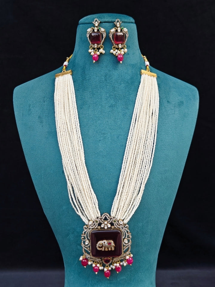 Close-up of an ornate traditional Ruby Pink (Mehendi Polish) Colored Stone jewellery set and earrings with American Diamond, Ruby Pink Colored Stones, Tumble Beads, Kundan and Pearls. Mehendi function outfit styled with a lightweight American Diamond necklace.