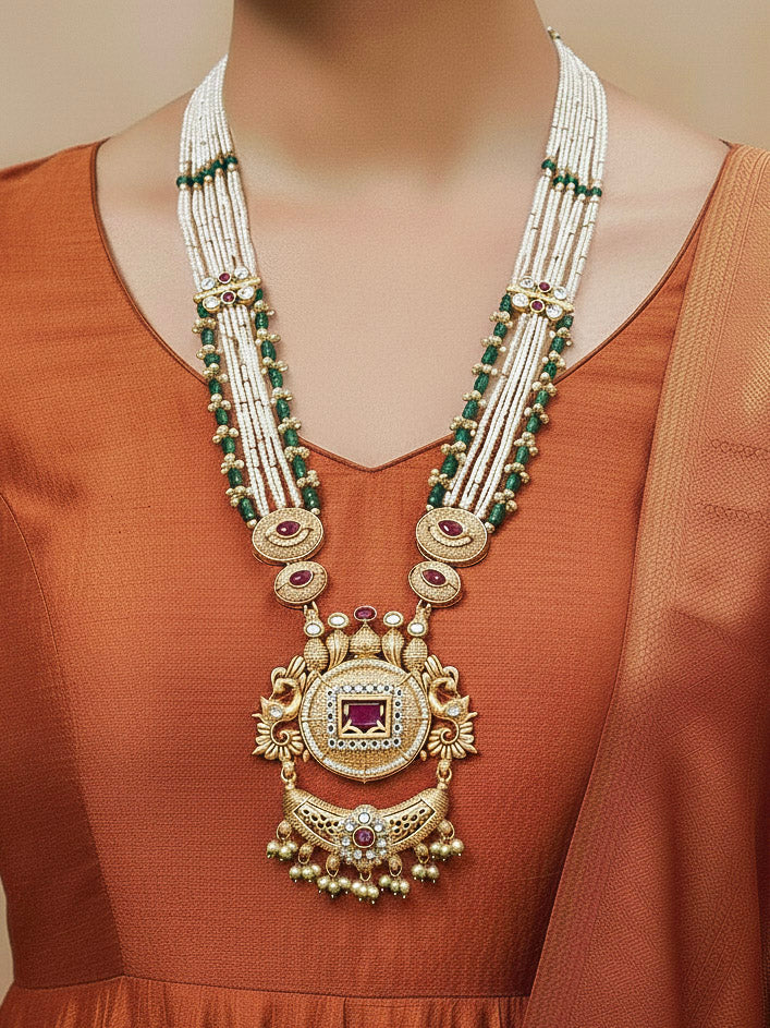 Close-up of a woman wearing an ornate traditional Red and Green Rajwadi gold Long jewellery set and earrings  with  Pearls, Beads, Ruby Red Colored Stones  and Bandhai Work. Mehendi ceremony look styled with a Rajwadi artificial jewelry set. Festive Diwali outfit enhanced with a Rajwadi artificial necklace.