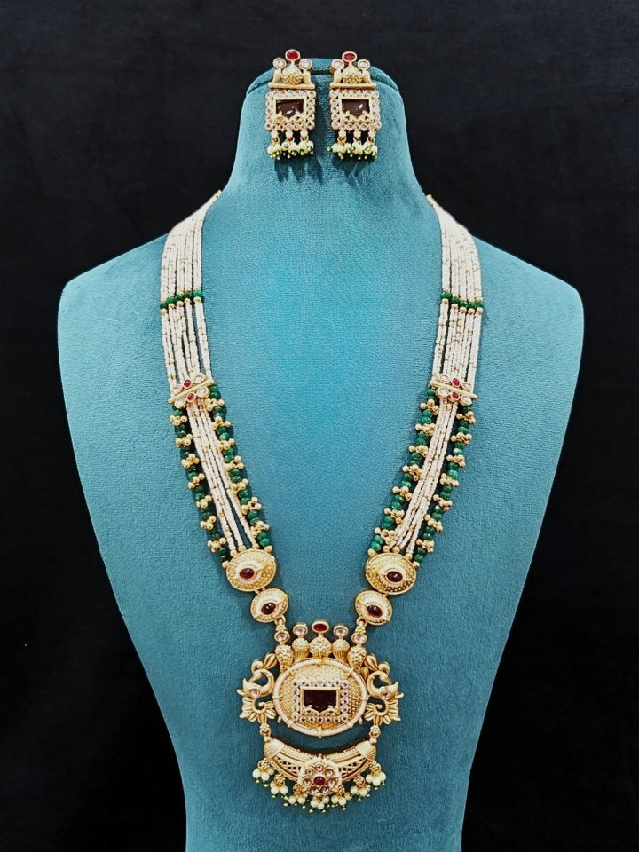 Close-up of a woman wearing an ornate traditional Red and Green Rajwadi gold Long jewellery set and earrings  with  Pearls, Beads, Ruby Red Colored Stones  and Bandhai Work. Mehendi ceremony look styled with a Rajwadi artificial jewelry set. Festive Diwali outfit enhanced with a Rajwadi artificial necklace.