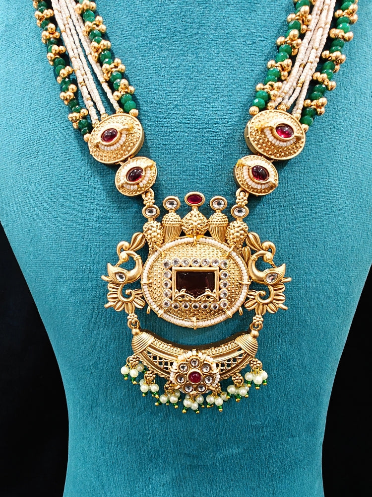 Close-up of a woman wearing an ornate traditional Red and Green Rajwadi gold Long jewellery set and earrings  with  Pearls, Beads, Ruby Red Colored Stones  and Bandhai Work. Mehendi ceremony look styled with a Rajwadi artificial jewelry set. Festive Diwali outfit enhanced with a Rajwadi artificial necklace.