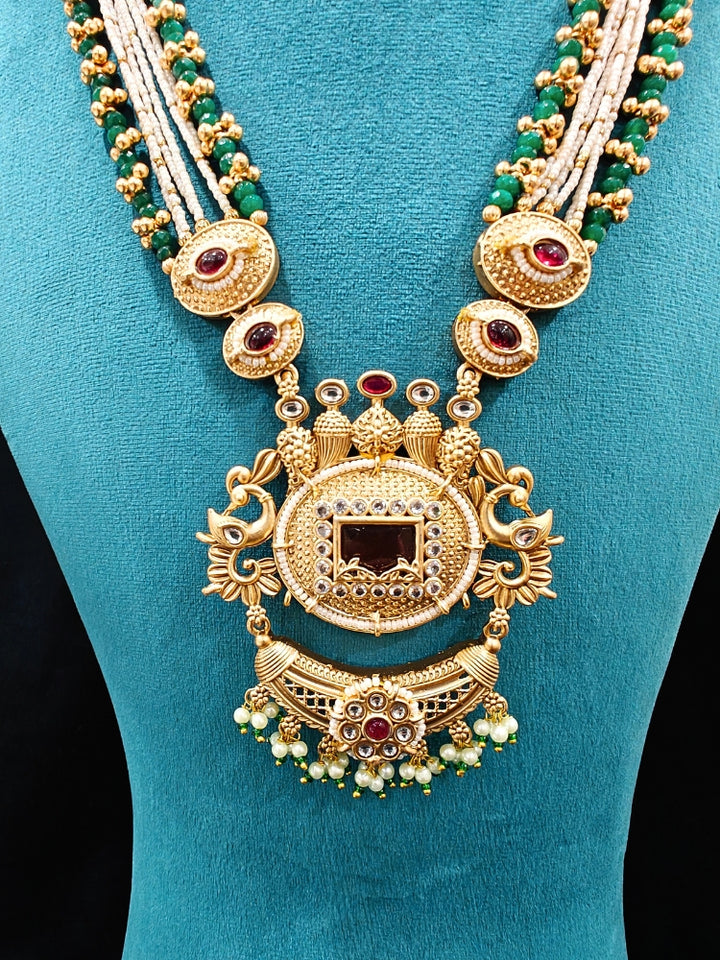 Close-up of a woman wearing an ornate traditional Red and Green Rajwadi gold Long jewellery set and earrings  with  Pearls, Beads, Ruby Red Colored Stones  and Bandhai Work. Mehendi ceremony look styled with a Rajwadi artificial jewelry set. Festive Diwali outfit enhanced with a Rajwadi artificial necklace.