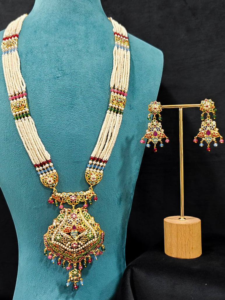 Close-up of an ornate traditional Navratan long jadau gold jewellery set and jadau earrings with pearls and gemstones. Elegant reception look featuring a luxury Jadau artificial jewelry set. Bridal styling inspiration with a premium Jadau imitation necklace.