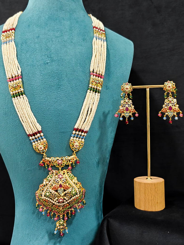 Close-up of an ornate traditional Navratan long jadau gold jewellery set and jadau earrings with pearls and gemstones. Elegant reception look featuring a luxury Jadau artificial jewelry set. Bridal styling inspiration with a premium Jadau imitation necklace.
