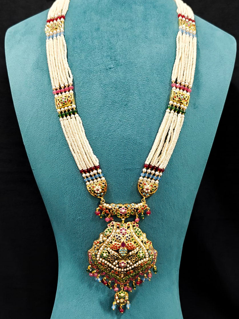 Close-up of an ornate traditional Navratan long jadau gold jewellery set and jadau earrings with pearls and gemstones. Elegant reception look featuring a luxury Jadau artificial jewelry set. Bridal styling inspiration with a premium Jadau imitation necklace.