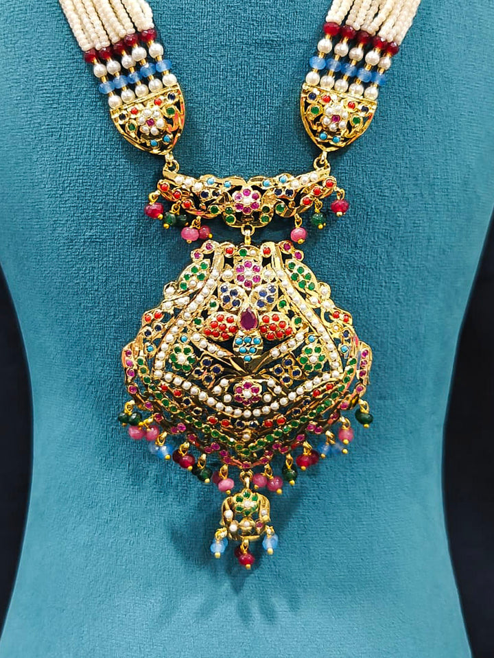 Close-up of an ornate traditional Navratan long jadau gold jewellery set and jadau earrings with pearls and gemstones. Elegant reception look featuring a luxury Jadau artificial jewelry set. Bridal styling inspiration with a premium Jadau imitation necklace.