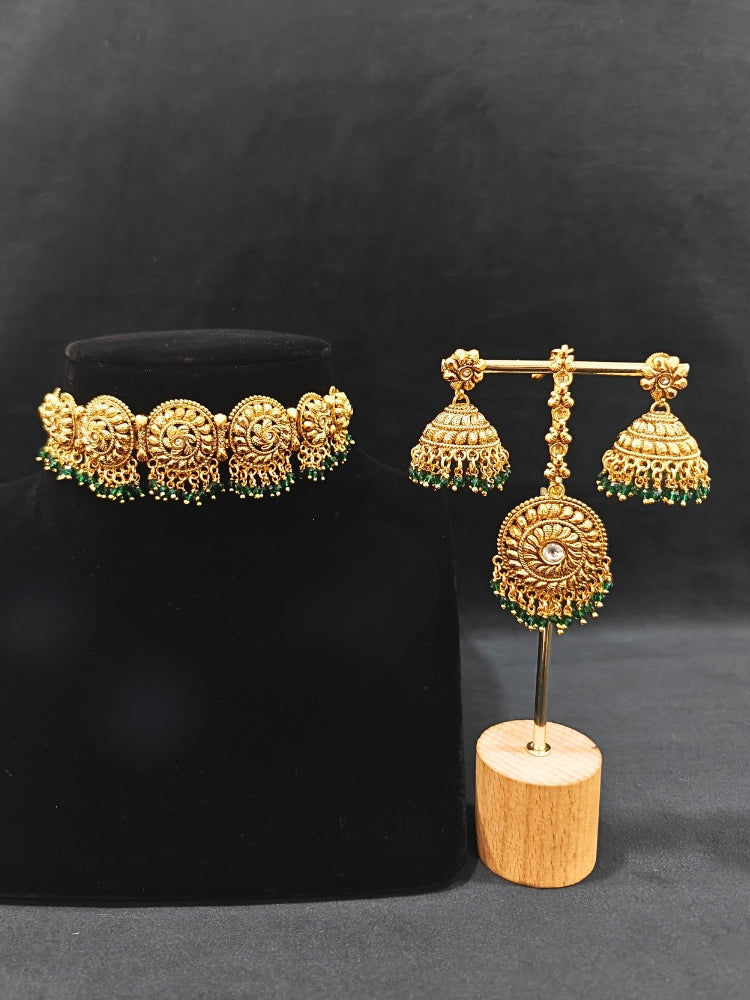 Close-up of an ornate traditional (Gold Polish) Choker jewellery set and earrings and maangtikka with Green Crystal Beads. Woman wearing a luxury artificial jewelry set styled for an Indian wedding celebration. Wedding celebration styling with a luxury artificial  jewelry design.