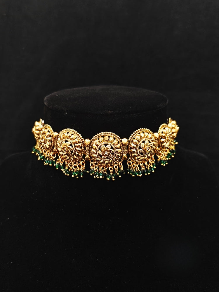 Close-up of an ornate traditional (Gold Polish) Choker jewellery set and earrings and maangtikka with Green Crystal Beads. Woman wearing a luxury artificial jewelry set styled for an Indian wedding celebration. Wedding celebration styling with a luxury artificial  jewelry design.
