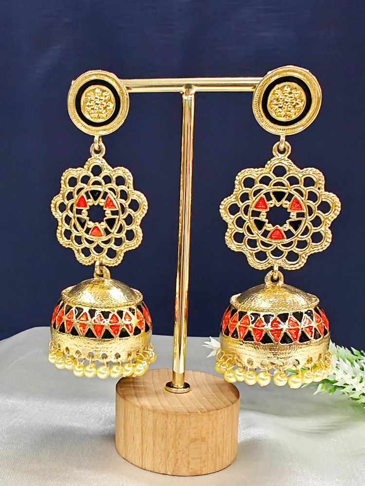 The Suhani Earrings are ornate gold and red jhumka earrings featuring intricate filigree, dome-shaped drops, and small gold beads, elegantly presented on a gold stand with a wooden base against a dark background.