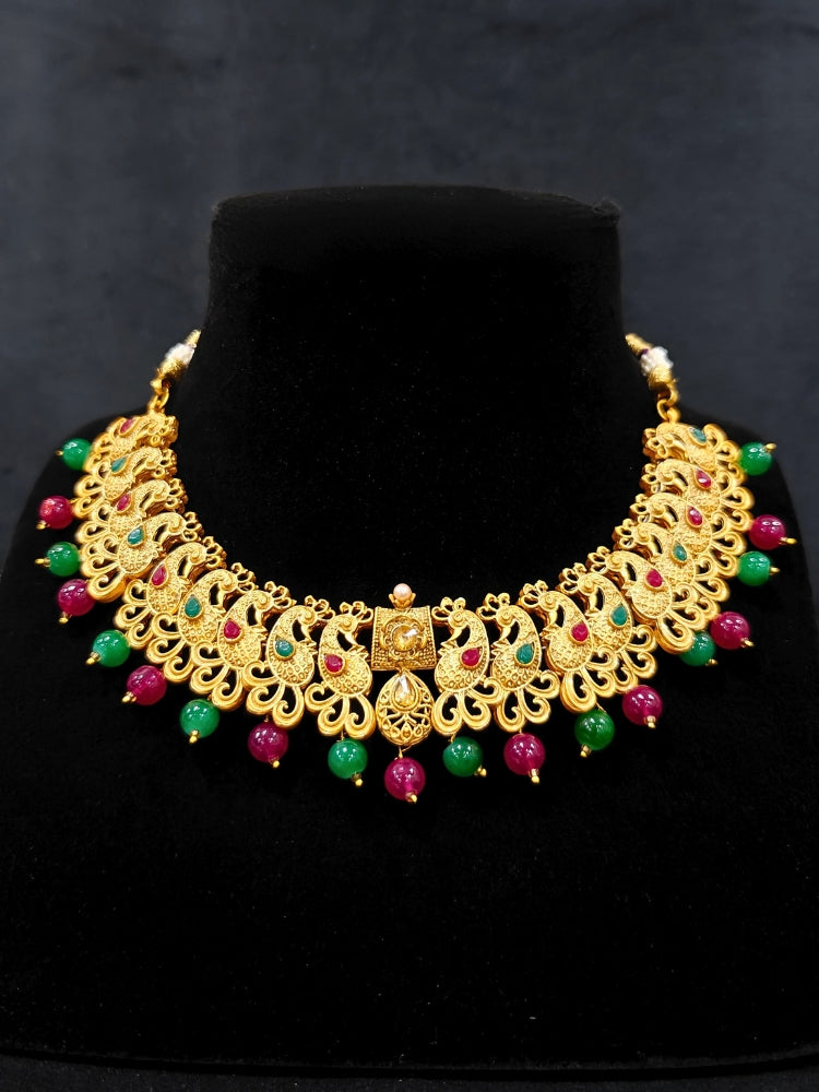Close-up of an ornate traditional (Gold Polish) Collar jewellery set and earrings and maangtikka with Red & Green Colored Stone and Beads. Festive party wear look featuring a statement artificial Colored Stone jewelry piece. Woman wearing lightweight artificial Colored Stone jewelry for long wedding functions.