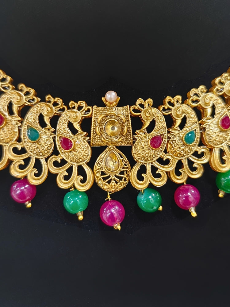Close-up of an ornate traditional (Gold Polish) Collar jewellery set and earrings and maangtikka with Red & Green Colored Stone and Beads. Festive party wear look featuring a statement artificial Colored Stone jewelry piece. Woman wearing lightweight artificial Colored Stone jewelry for long wedding functions.