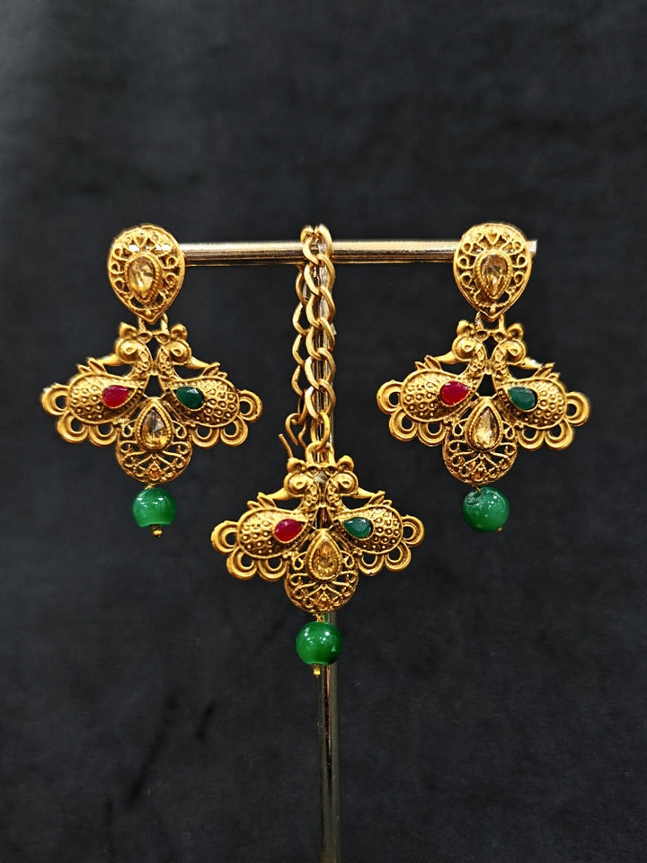 Close-up of an ornate traditional (Gold Polish) Collar jewellery set and earrings and maangtikka with Red & Green Colored Stone and Beads. Festive party wear look featuring a statement artificial Colored Stone jewelry piece. Woman wearing lightweight artificial Colored Stone jewelry for long wedding functions.