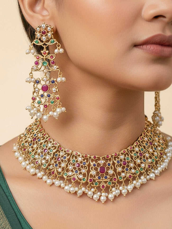 Close-up of a woman wearing an ornate traditional collar Navratan jadau gold jewellery set and jadau earrings with pearls and Navratan gemstones. Woman wearing a premium Jadau artificial jewelry set for reception night. Bridal styling inspiration with a premium Jadau imitation necklace.