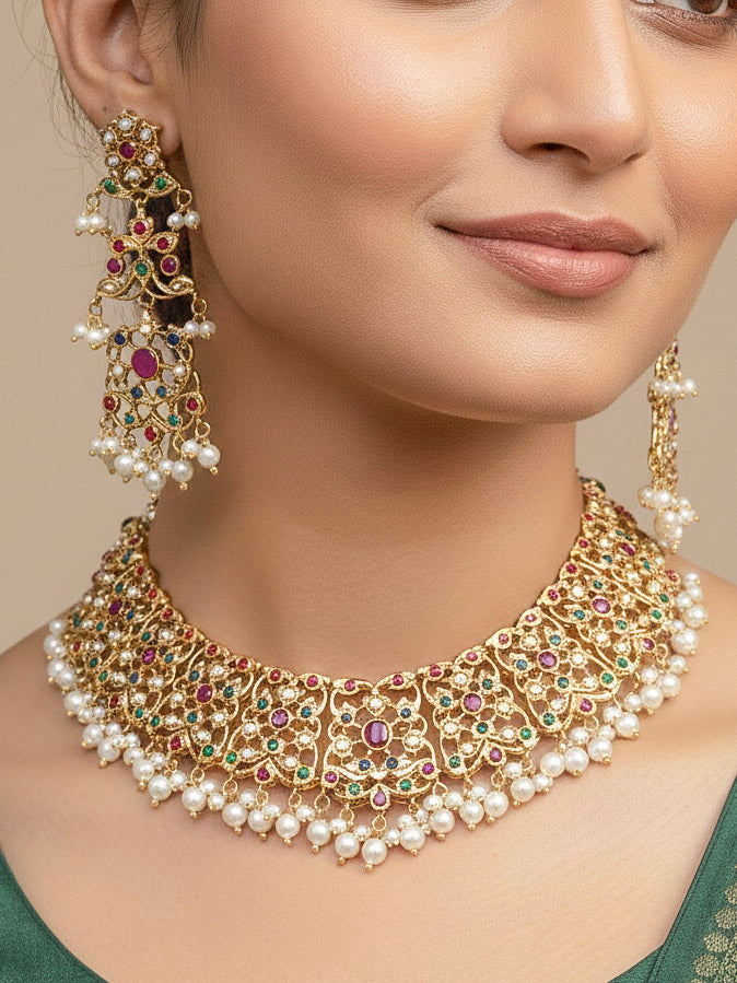 Close-up of a woman wearing an ornate traditional collar Navratan jadau gold jewellery set and jadau earrings with pearls and Navratan gemstones. Woman wearing a premium Jadau artificial jewelry set for reception night. Close-up of intricate Jadau detailing in artificial bridal jewelry.