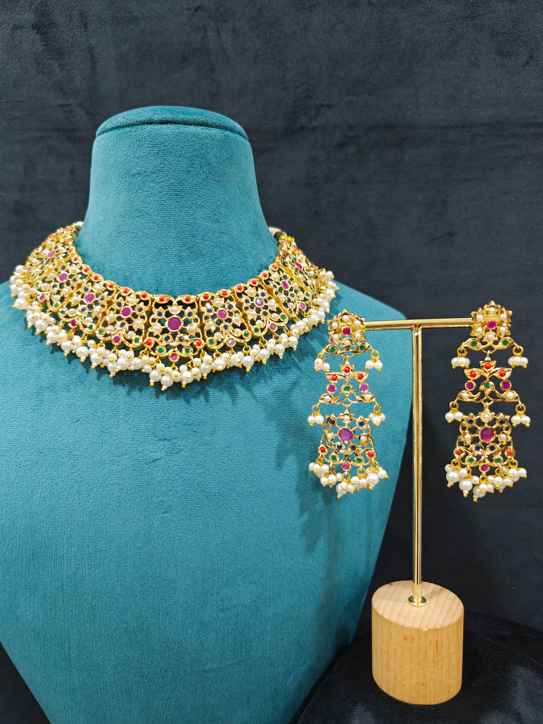 Close-up of an ornate traditional collar Navratan jadau gold jewellery set and jadau earrings with pearls and Navratan gemstones. Statement Jadau necklace styled for a wedding guest outfit. Close-up of intricate Jadau detailing in artificial bridal jewelry.