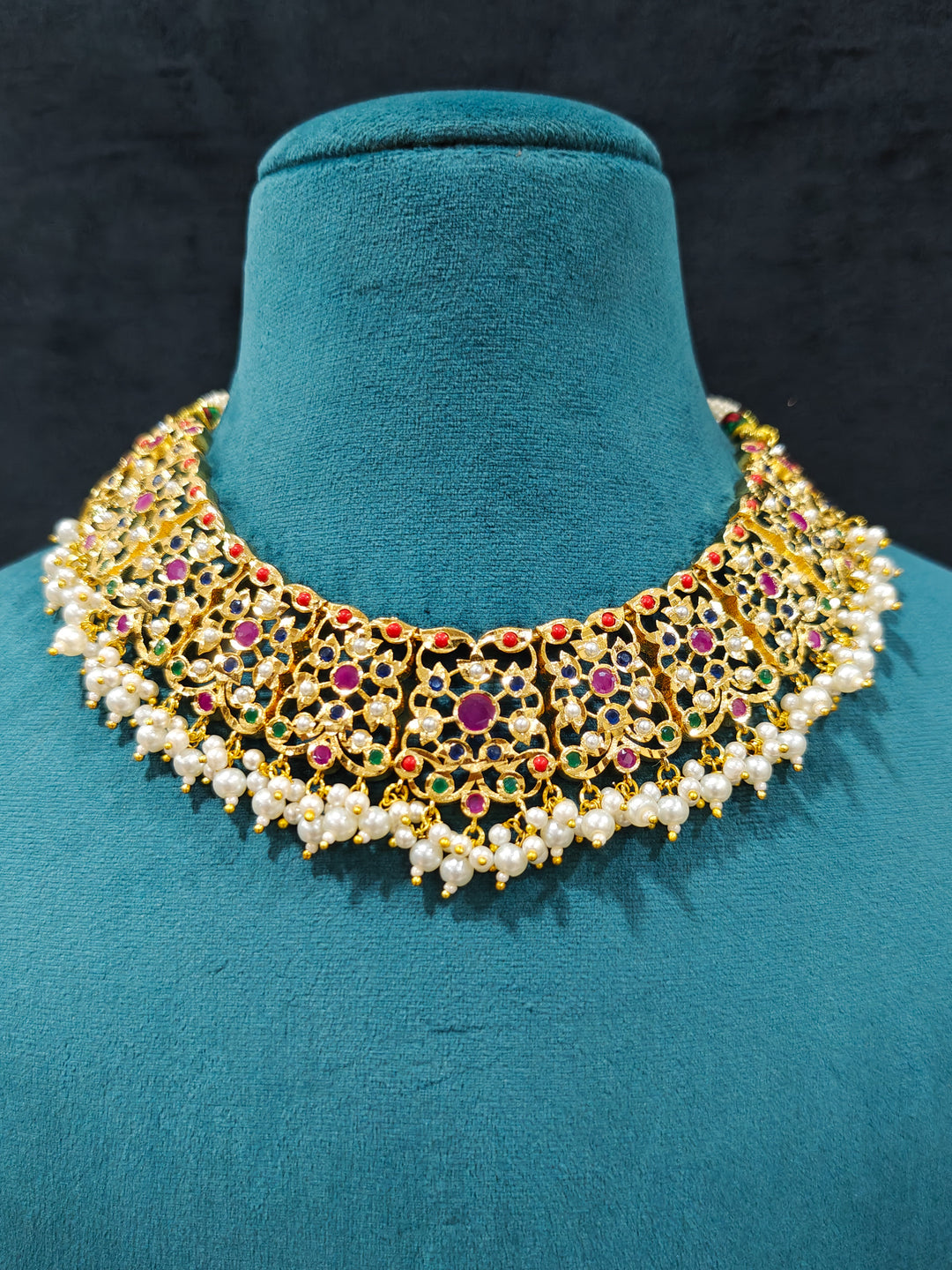 Close-up of an ornate traditional collar Navratan jadau gold jewellery set and jadau earrings with pearls and Navratan gemstones. Close-up of a Jadau artificial necklace for wedding celebrations. Close-up of intricate Jadau detailing in artificial bridal jewelry.
