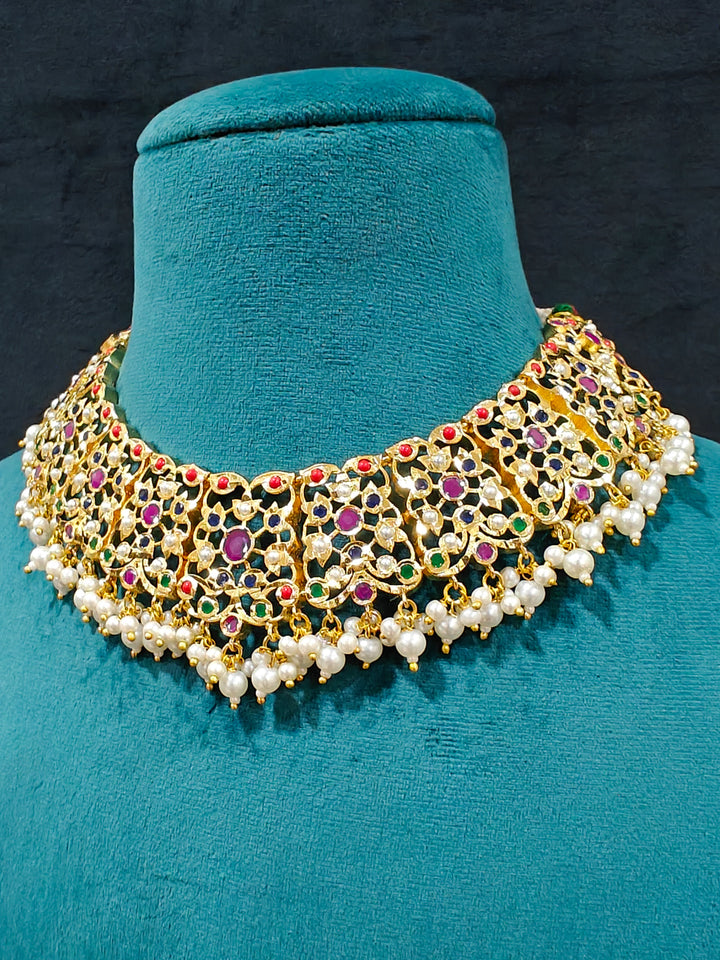 Close-up of an ornate traditional collar Navratan jadau gold jewellery set and jadau earrings with pearls and Navratan gemstones. Close-up of a Jadau artificial necklace for wedding celebrations. Close-up of intricate Jadau detailing in artificial bridal jewelry.